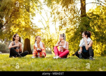 Vier schöne motivierte weibliche Freunde entspannend nach der Ausbildung in der Stadt parken. Stockfoto