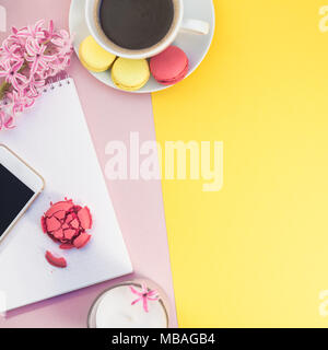 Kreative flach Foto von Kaffeetasse mit Makronen und einen Notizblock mit Kopie Raum auf Rosa und gelbem Hintergrund minimal Style Stockfoto