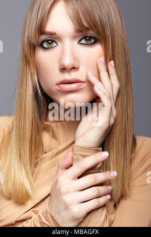 Porträt der blonde junge Frau. Frau mit grünen Augen und langes glattes Haar. Mädchen gekleidet in beige Kleid auf grauem Hintergrund. Stockfoto