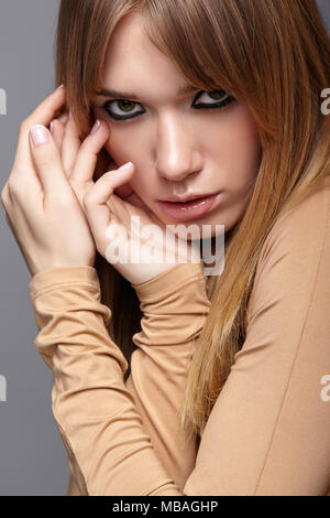 Porträt der blonde junge Frau. Frau mit grünen Augen und langes glattes Haar. Mädchen gekleidet in beige Kleid auf grauem Hintergrund. Stockfoto