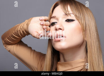 Porträt der blonde junge Frau. Frau mit grünen Augen und langes glattes Haar. Mädchen gekleidet in beige Kleid auf grauem Hintergrund. Stockfoto