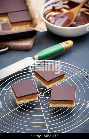 Caramel Shortbread/Millionäre shortbread Quadrate mit einem Palettenmesser auf einem runden vintage Gitter auf einer Schiefertafel Hintergrund Stockfoto