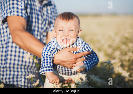 Closeup Portrait von Lustig fröhlich lachend zahnlos kaukasische Baby in den Händen der starken Papa. Vater werfen niedliche emotionale kleines Baby hoch in der Luft. Hor Stockfoto