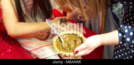 Weibliche Hände dekorativ durch Henna mit Schale gefärbt. Eine Schüssel mit Kokosnuss unter ihre Hand halten. Mischen Henna für die Haare. Natürliche henna Farbe gemischt in einer Schüssel eingefügt. Stockfoto