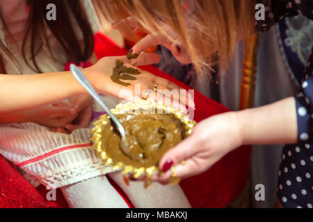 Weibliche Hände dekorativ durch Henna mit Schale gefärbt. Eine Schüssel mit Kokosnuss unter ihre Hand halten. Mischen Henna für die Haare. Natürliche henna Farbe gemischt in einer Schüssel eingefügt. Stockfoto