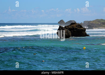 Wellen zwischen den Felsen an der Küste des Karibischen Meeres mit einem gelben Schwimmer im Wasser brechen Stockfoto