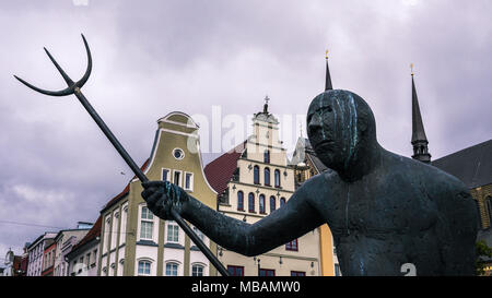 Eine eindrucksvolle Statue Winkel a Trident auf dem Weg zu einem ominösen Sky auf dem Platz der Stadt Rostock, die erhaltenen Hafenstadt im Norden Deutschlands. Stockfoto