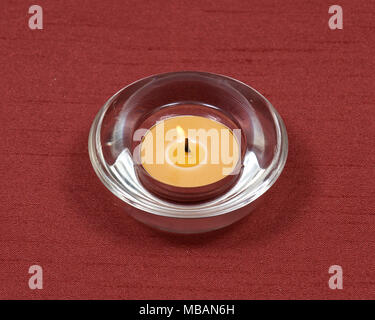 Brennen gelb Kerze aus Bienenwachs in Quarz Schüssel auf rotem Stoff Hintergrund Stockfoto