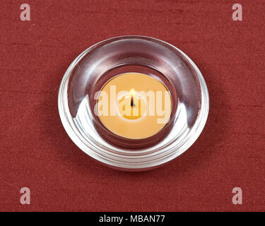 Brennen gelb Kerze aus Bienenwachs in Quarz Schüssel auf rotem Stoff Hintergrund Stockfoto