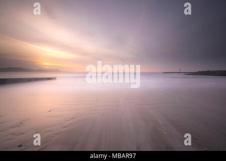 Schöne rosa Töne in den Himmel und Meer bei Sonnenaufgang als morgen Wellen sanft Rolle auf dem Sandstrand in Lyme Regis. Stockfoto