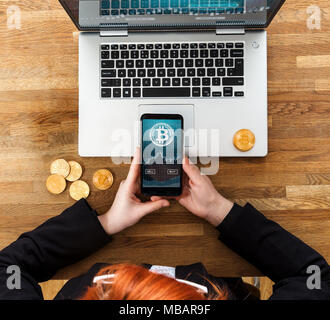 Menschen mit Smartphone App bitcoins zu kaufen oder zu verkaufen. Laptop und Goldmünzen der BTC auf Tisch. Stockfoto