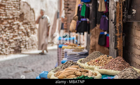 Stapel von Gewürzen und Kräutern in großen Körben vor einem Spice Shop in Marrakesch, Marokko. Einen marokkanischen Mann in die djellaba ist zu Fuß in den ​Background. Stockfoto