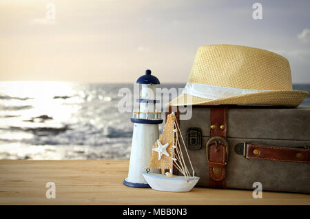 Traveler vintage Gepäck, Boot und fedora Hut über holztisch vor Meer Landschaft bei Sonnenuntergang. Urlaub und Ferienhäuser Konzept Stockfoto