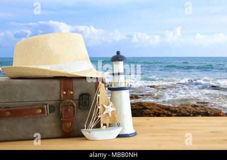 Traveler vintage Gepäck, Boot und fedora Hut über holztisch vor Meer Landschaft. Urlaub und Ferienhäuser Konzept Stockfoto