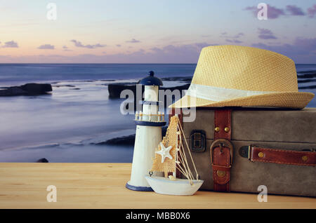 Traveler vintage Gepäck, Boot und fedora Hut über holztisch vor Meer Landschaft bei Sonnenuntergang. Urlaub und Ferienhäuser Konzept Stockfoto