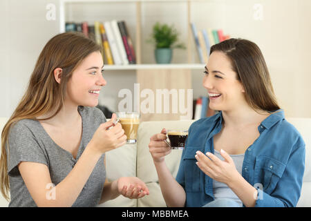 Zwei glückliche Freunde reden und trinken Kaffee auf einer Couch im Wohnzimmer zu Hause sitzen Stockfoto