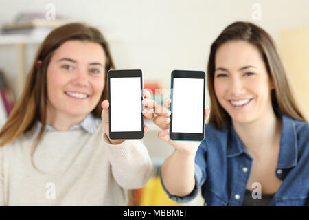 Zwei glückliche Schüler zeigen ihre beiden smart phone Bildschirme auf die Kamera zu Hause Stockfoto