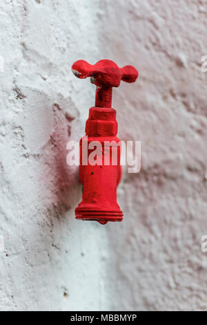 Metallische Wasserhahn rot lackiert auf eine raue weiße Wand Stockfoto