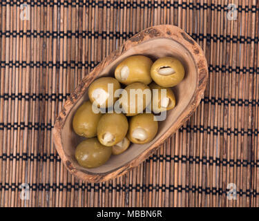 Grüne kolossale Oliven gefüllt mit Knoblauch Handschuhe Hand in Olivenholz Schüssel Stockfoto