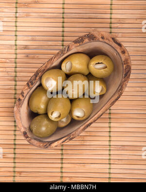 Grüne kolossale Oliven gefüllt mit Knoblauch Handschuhe Hand in Olivenholz Schüssel Stockfoto