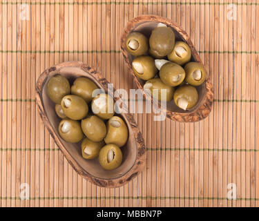 Grüne kolossale Oliven gefüllt mit Knoblauch Handschuhe Hand in Olivenholz Schüssel Stockfoto