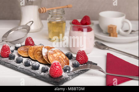 Mini Pfannkuchen mit Obst und Honig auf einem Teller mit Joghurt und Honig im Hintergrund Stockfoto