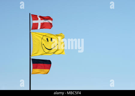 Deutsche und dänische Flaggen schwenkten zusammen mit einem Smiley Flagge an einem Fahnenmast Stockfoto