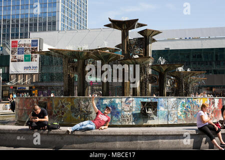 Ein junger Mann nimmt einen selfie am Alexanderplatz Brunnen der Völkerfreundschaft (Brunnen der Freundschaft) in der ehemaligen DDR Berlin, Deutschland. Stockfoto