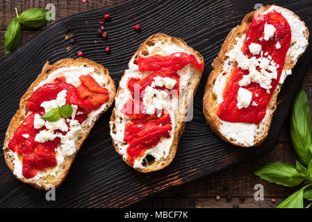 Bruschetta mit geröstetem Paprika, Feta Käse und Olivenöl auf alten hölzernen Schneidebrett, Ansicht von oben. Italienische Küche Vorspeisen, Starter oder Antipasti Stockfoto