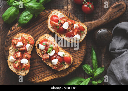 Italienische Antipasti, Bruschetta mit Tomaten, Mozzarella und Basilikum auf Holzbrett. Ansicht von oben, getönten Bild Stockfoto