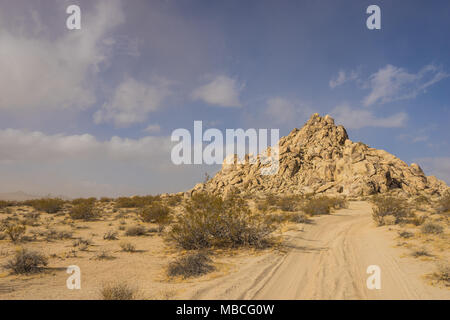 Weicher Sand Straße führt durch die Wüste zu einem massiven Hill aus Sandstein Felsbrocken. Stockfoto