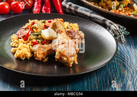 Traditionelle Paella mit Huhn Beine, Chorizo Wurst und Gemüse auf schwarzem Teller serviert. Spanische Küche Stockfoto