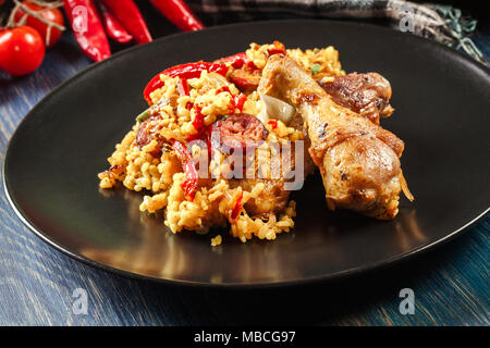 Traditionelle Paella mit Huhn Beine, Chorizo Wurst und Gemüse auf schwarzem Teller serviert. Spanische Küche Stockfoto