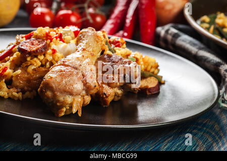 Traditionelle Paella mit Huhn Beine, Chorizo Wurst und Gemüse auf schwarzem Teller serviert. Spanische Küche Stockfoto