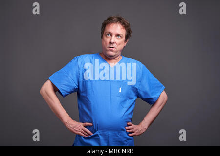 Ein Männer mittleren Alters Arzt stehen in einem blauen Schrubben und Langeweile Stockfoto