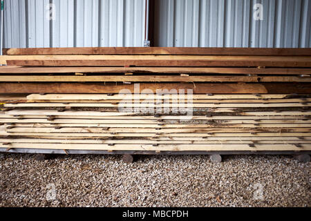 Frisch geschnitten oder gefräst rauhes Bauholz Bretter ordentlich in einem Yard gestapelt in einem Holz Mühle außerhalb einer Metall Wand des Lagerhauses Stockfoto