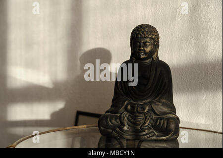 Buddha Statue auf dem Tisch auf dem Hintergrund Wand mit Schatten. Stockfoto