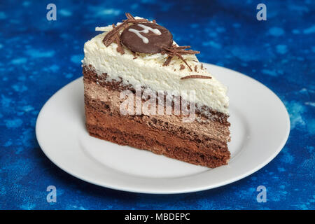 Stück leckere Mousse Cake mit drei verschiedenen Arten von Schokolade auf weiße Platte. Blauer Hintergrund Stockfoto