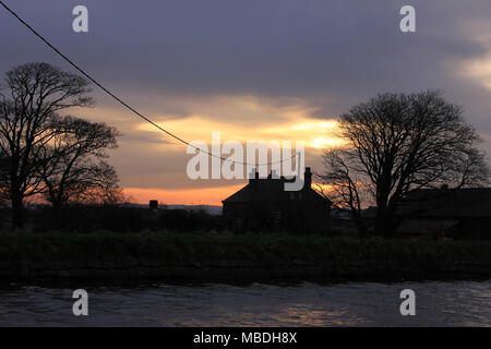 Gleich nach der Dämmerung am Freitag den 6.4.18 eine schwache Sonne hinter Holz House Farm in der Nähe von burscough in West Lancashire steigt. Stockfoto