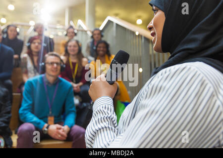 Lächelnd Geschäftsfrau im hijab Rede vor Publikum mit Mikrofon Stockfoto