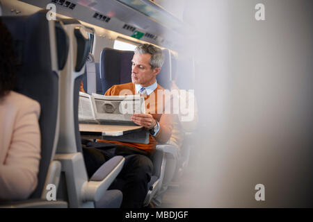 Geschäftsmann lesen Zeitung auf Personenzug Stockfoto