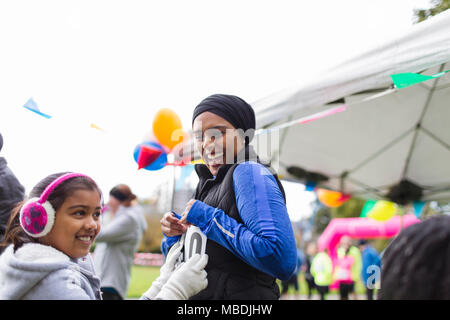 Lächelnd Tochter pinning Marathon bib auf Mutter an der Nächstenliebe ausführen Stockfoto