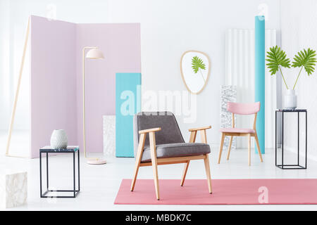 Grau Sessel in einer pastellfarbenen Zimmer Innenraum mit rotem Teppich, pink Stuhl, Metall Beistelltisch und Blätter Stockfoto