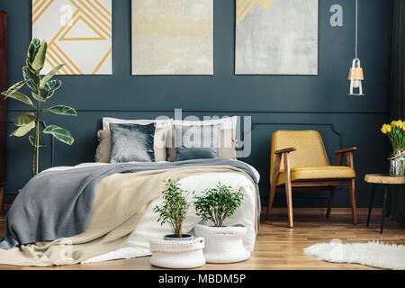 Vintage Schlafzimmer Innenraum mit retro Stuhl, blau und grau Decken, Kissen, Pflanzen, weißer Teppich und modernen Gemälden Stockfoto