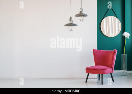 Lampen über dem roten Stuhl und Löwenzahn gegen grüne Wand mit runder Spiegel in Wohnzimmer Innenraum Stockfoto