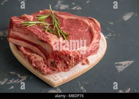 Schneiden von Fleisch zum Grillen auf Holz Schneidebrett mit Lorbeerblatt, Rosmarin für die Marinade in einer rustikalen Stil. Kopieren Sie Platz. Ein horizontaler Rahmen. Stockfoto