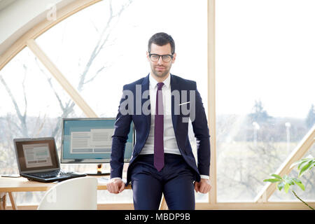 Portrait der junge Unternehmer tragen Anzug und mit Blick auf die Kamera beim Sitzen am Schreibtisch und Blick auf Kamera. Stockfoto
