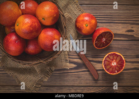 Blut orange Frucht in einem Weidenkorb und Flasche Saft auf dunklen Holztisch. Dunklen rustikalen Stil. Ansicht von oben. Stockfoto