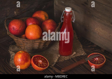 Blut orange Frucht in einem Weidenkorb und Flasche Saft auf dunklen Holztisch. Dunklen rustikalen Stil. Stockfoto