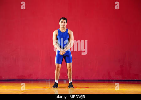 Junger Mann Greco-römischen Wrestler in blauen Uniform stehend auf einem gelben wrestling Teppich in der Turnhalle Stockfoto